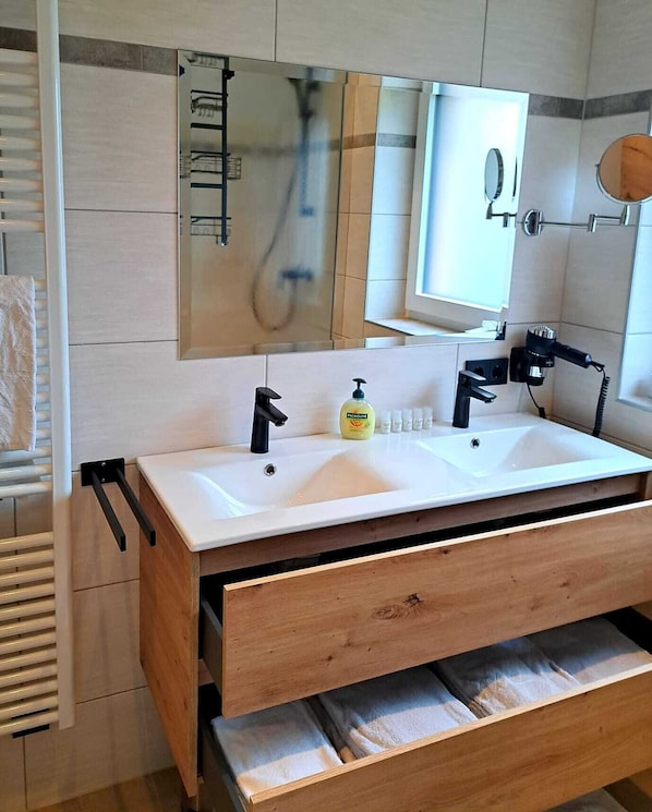A modern bathroom with a double sink, a mirror, a towel rack, and a wooden vanity with drawers.