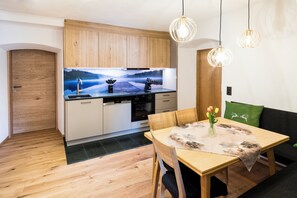 A modern kitchen with wooden cabinets, a dining table with a placemat, and a sofa with a green cushion. - Gasthof Knappenwirt (Neumarkt in Steiermark)