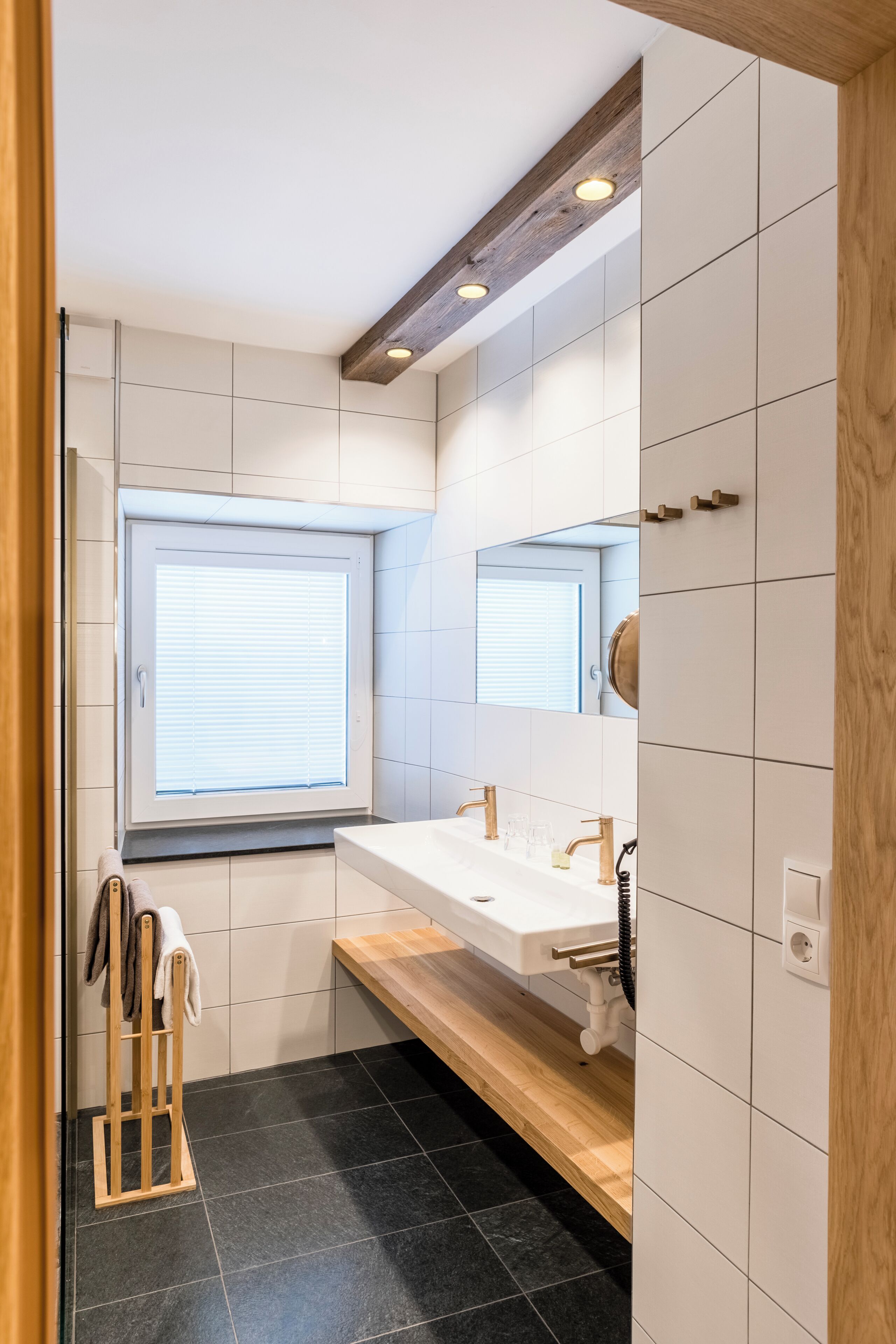 Un baño moderno con un ventanal grande, un banco de madera y un lavamanos blanco.