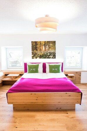 A bedroom with a wooden bed, a large window with blinds, a ceiling light fixture, and a wall-mounted painting. - Gasthof Knappenwirt (Neumarkt in Steiermark)