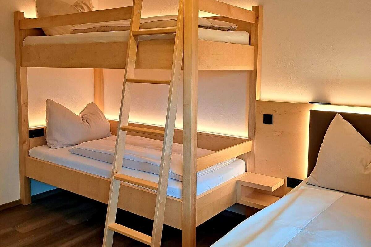 Una cama litera con escalera de madera, una mesita de noche y una lámpara fijada a la pared.