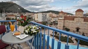 Un balcon avec une table dressée pour le petit-déjeuner, d’où l’on peut admirer un panorama urbain avec des bâtiments historiques et une colline en arrière-plan.
