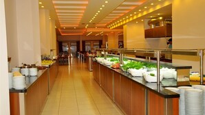 A buffet area with multiple food stations, including salads and fruits, and a long counter with stacked plates. - Blue Fish (Alanya)