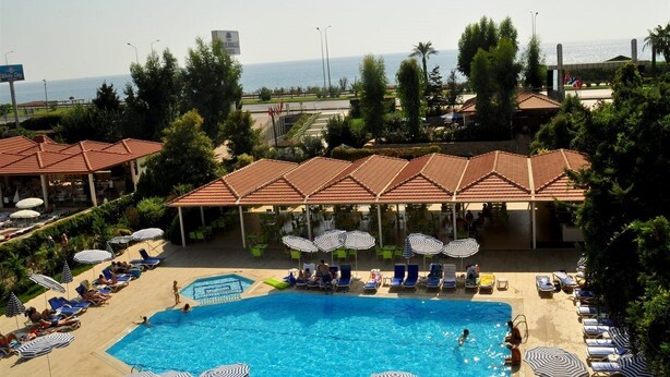 A hotel pool area with sun loungers and umbrellas, a covered seating area, and a view of the sea. - Blue Fish (Alanya)