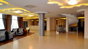A spacious lobby with a modern design, featuring a central column with mosaic tiles, a spiral staircase, and a seating area with sofas and armchairs. - Blue Fish (Alanya)