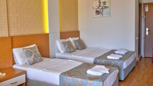 A hotel room with two beds, a wooden headboard, a nightstand, and a wall-mounted artwork. - Blue Fish (Alanya)