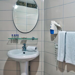 Een badkamer met een wit wastafelmeubel, een spiegel, een handdoekhouder en een haardroger.