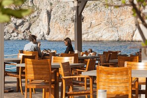 A coastal restaurant with wooden tables and chairs, overlooking a rocky cliff and the sea. - Kyrimai Hotel (East Mani)