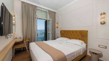 A hotel room with a bed, a desk, a chair, a TV, a window with curtains, and a balcony.
