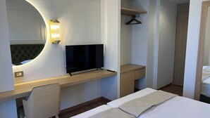 A hotel room with a bed, a desk with a TV, a chair, a wardrobe, and a mirror.