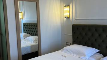 A hotel room with a large bed, a mirror, a wall-mounted light, and a door.