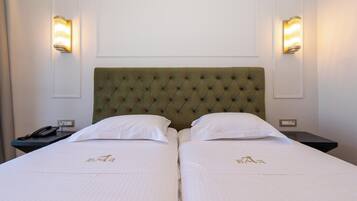 A hotel room with two beds, each with a tufted headboard and white linens. There are bedside tables with lamps and a phone on one of them.