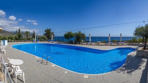 Una piscina con vistas claras al mar, rodeada de sillas de descanso y un muro de piedra.