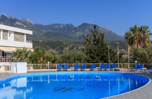 A swimming pool with a mountain backdrop, surrounded by lounge chairs and palm trees. - Kardamili Beach Hotel (West Mani)