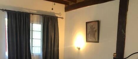 A bedroom with a large bed, a chair, a small table, and a wall-mounted light.