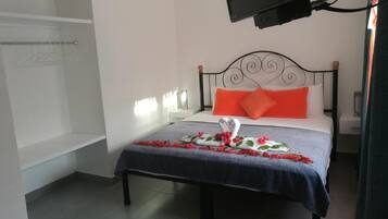 Une chambre d’hôtel comprenant un lit, une table de chevet, un téléviseur fixé au mur et un espace douche.