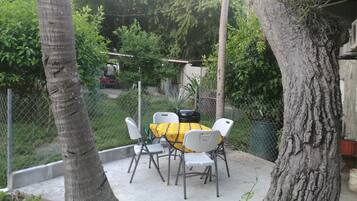 An outdoor patio with a table and chairs, surrounded by trees and a fence.
