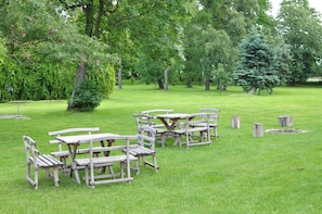 An outdoor seating area with wooden tables and benches, surrounded by lush greenery and trees.