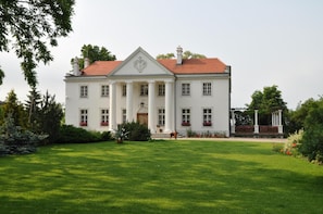 A large, white building with a symmetrical facade, a central entrance flanked by columns, and a red-tiled roof.
