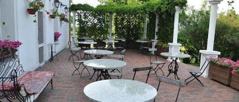 Un patio al aire libre con mesas y bancos redondos, rodeado de paredes blancas y follaje.