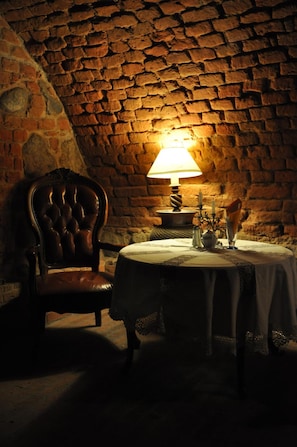 A dimly lit room with a stone wall, a table with a lamp, and a chair.