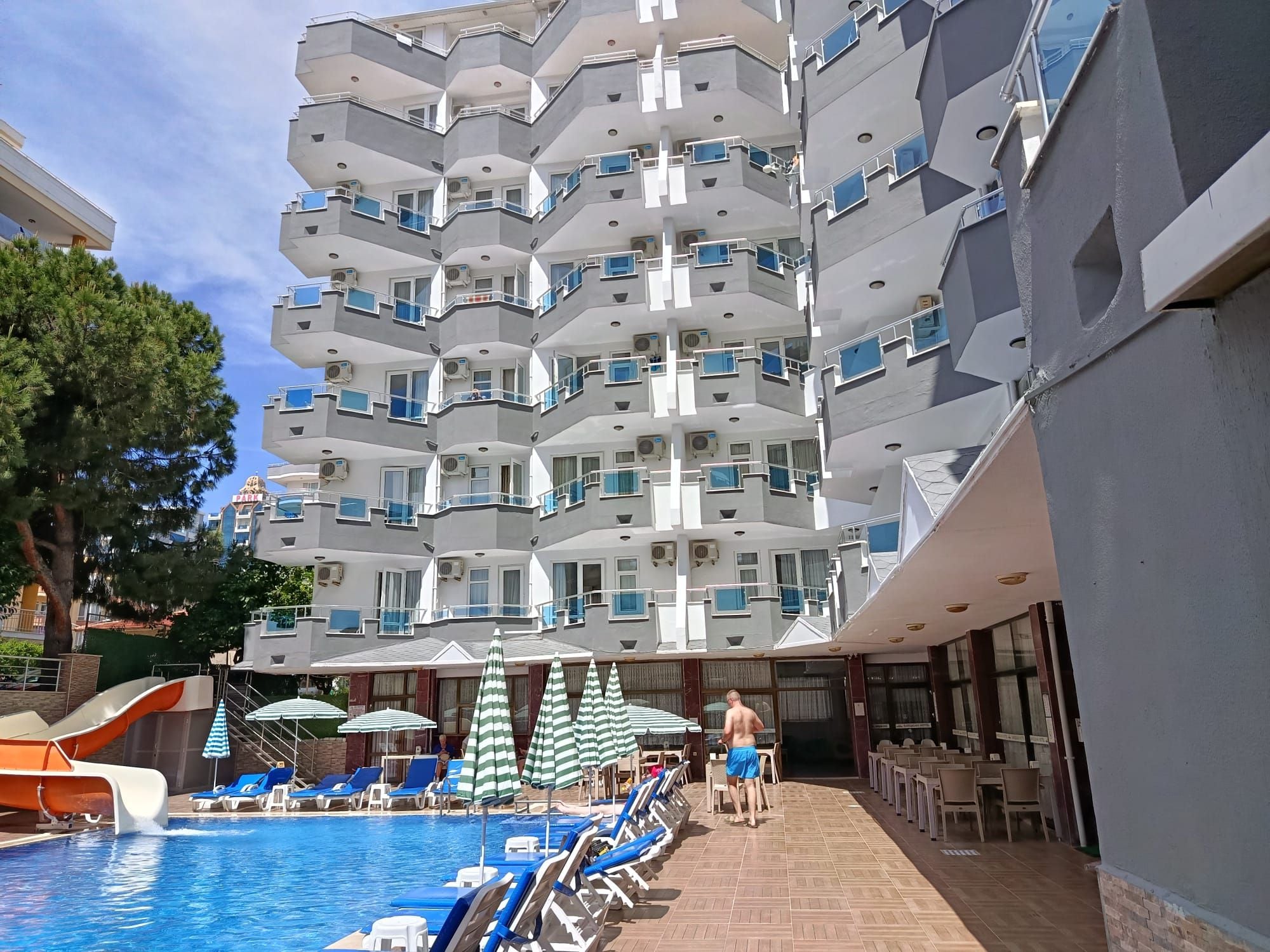 Un hôtel à plusieurs étages doté de balcons, d’un espace piscine avec des chaises longues et d’un coin salon extérieur.