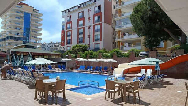 Zona de piscina con sillones de descanso, sombrillas y un tobogán.