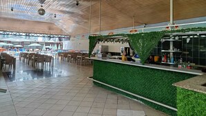 Un espacio interior amplio con techo alto, zona de bar con césped artificial verde y varias distribuciones de mobiliario.