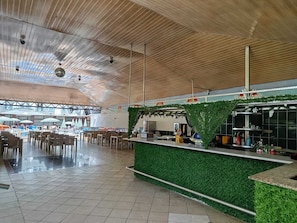 Espai interior ampli amb un sostre alt, zona de bar amb gespa artificial verda i un terra de rajola.