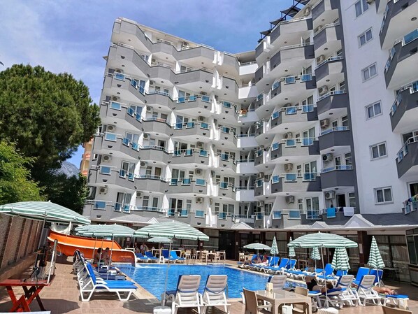 A multi-story hotel with a swimming pool, outdoor seating, and balconies.