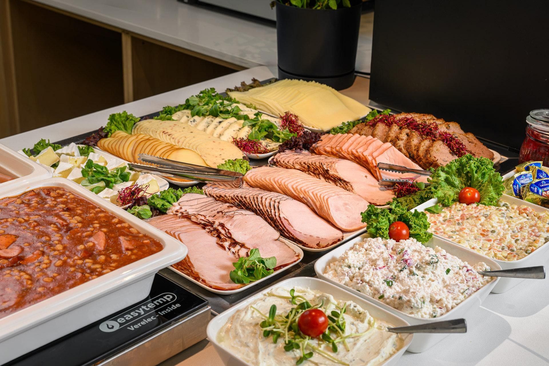 A buffet with various food items including sliced meats, cheeses, and salads.