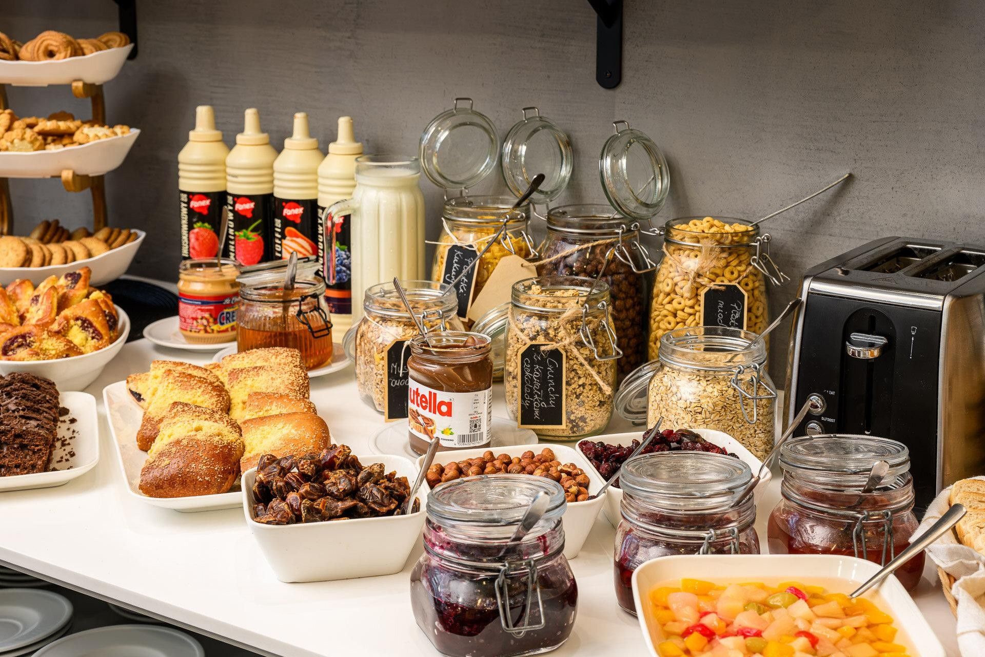 Un buffet proposant une variété d’aliments, notamment des pâtisseries, des fruits secs et des pots de confitures et de pâtes à tartiner.
