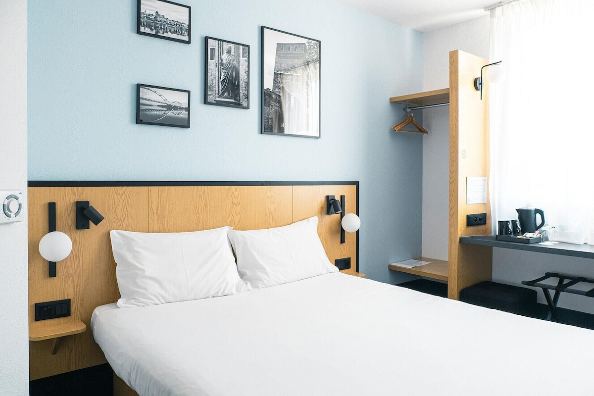 Habitación de hotel con cabecera de madera, ropa de cama blanca y escritorio con cafetera.