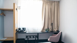 A hotel room with a bed, a desk with a chair, a coffee maker, a kettle, and a window with curtains. - B&B Hotel Torun (Torun)