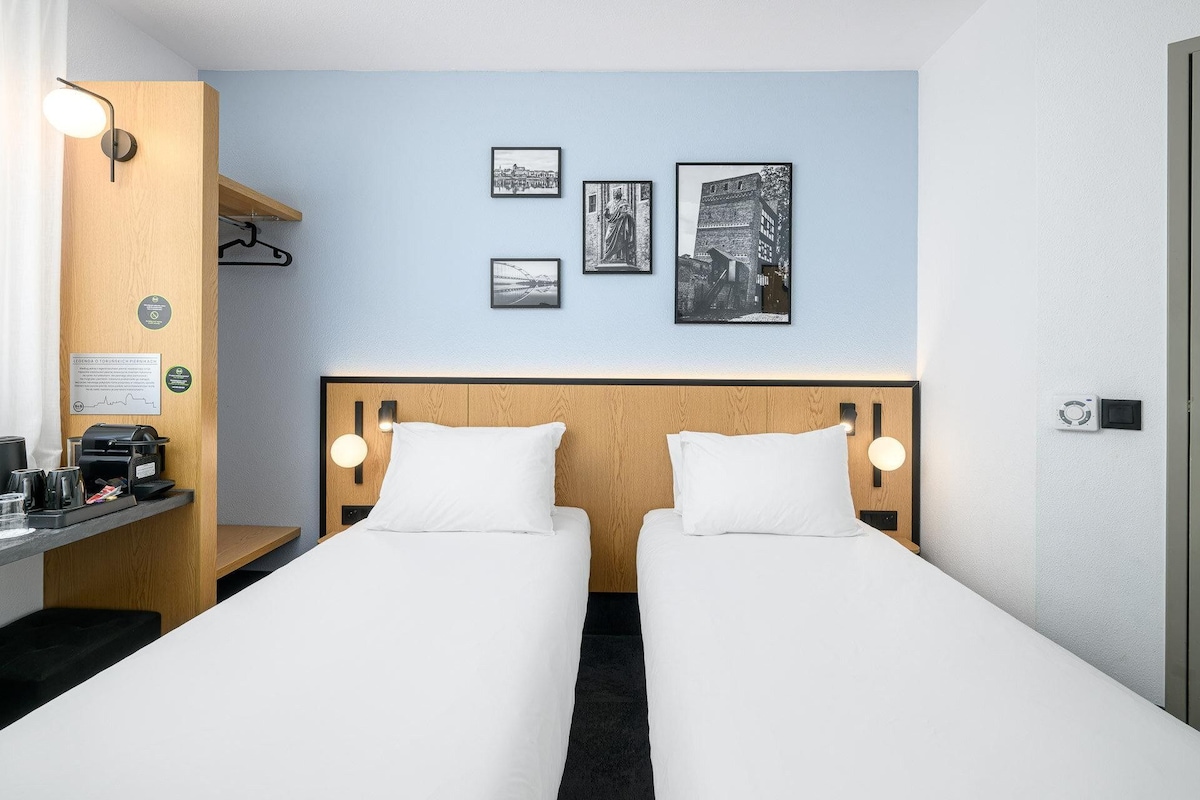 A hotel room with two beds, a desk with a coffee maker, and wall-mounted lights.