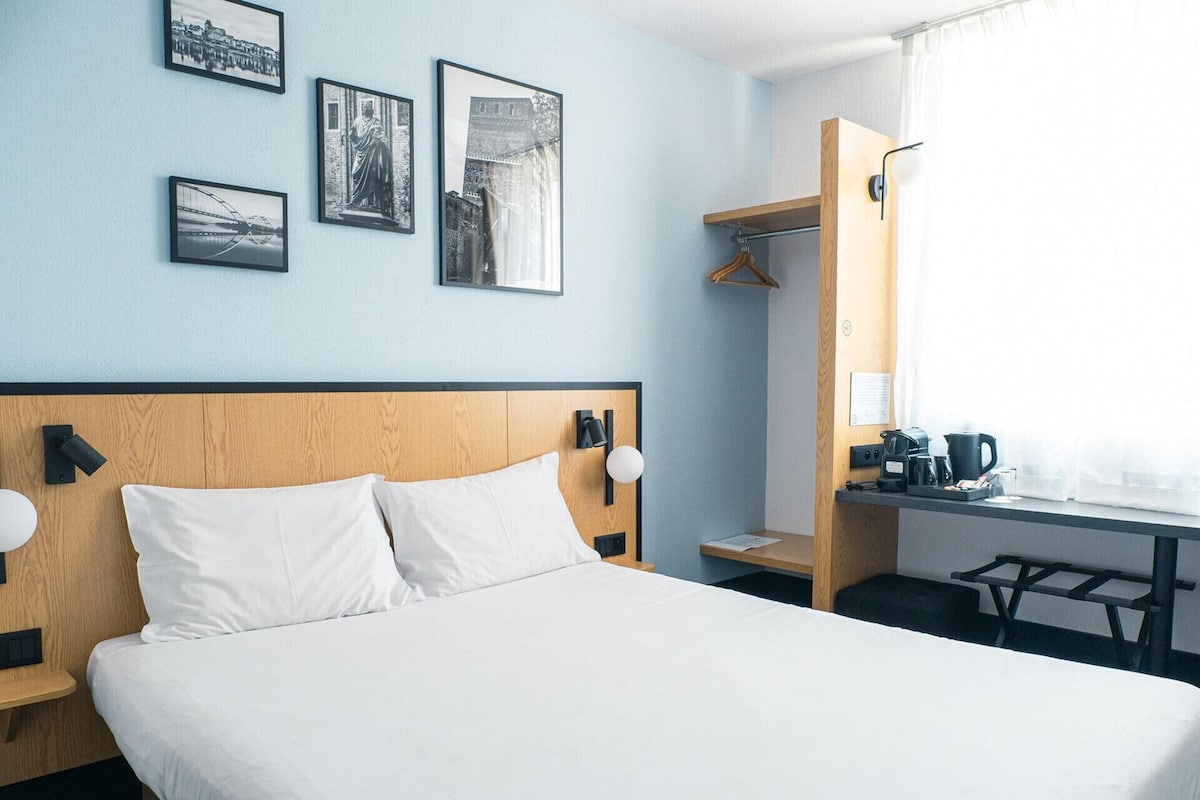 Una habitación de hotel con una cama, un escritorio con cafetera y un armario.