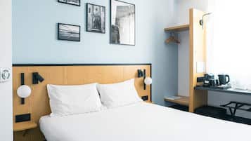Habitación de hotel con cabecera de madera, ropa de cama blanca, escritorio con cafetera y cuadros en la pared.
