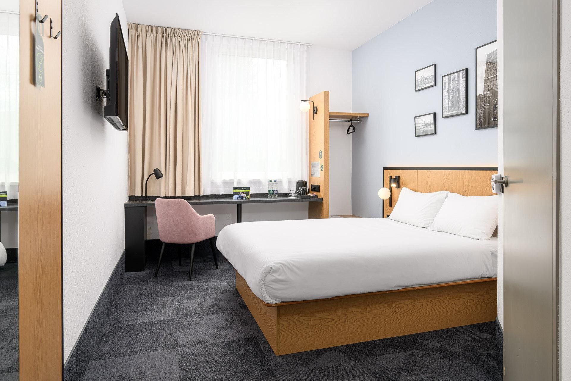 A hotel room with a bed, desk, chair, and a window with curtains.