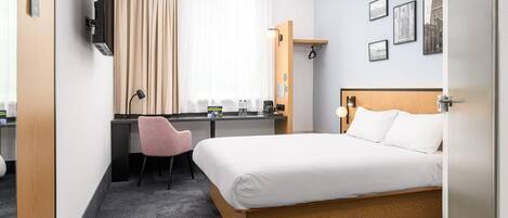 Habitación de hotel con cama, escritorio, silla y ventana con cortinas.