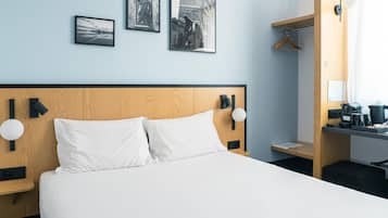 Habitación de hotel con cabecera de madera, ropa de cama blanca y tres fotografías blanco y negro en la pared.
