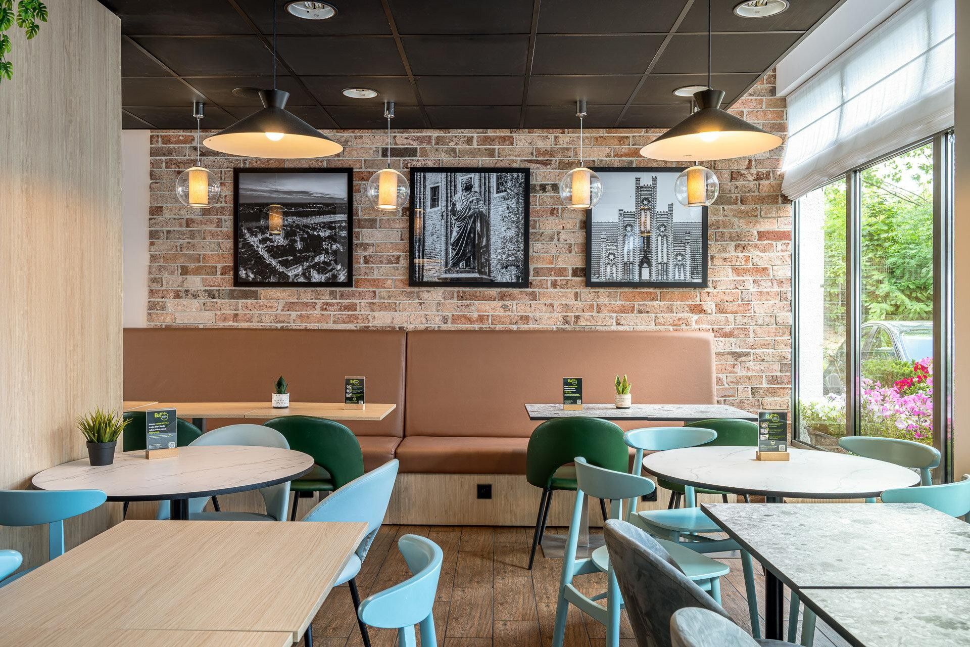 A restaurant interior with brick walls, round tables, green chairs, and pendant lighting.
