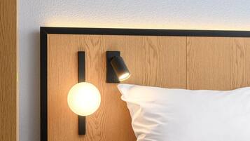A hotel room with a wooden headboard, a bedside table with a lamp, and a bed with white bedding.