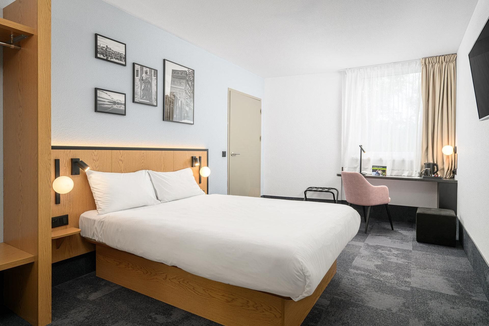 A hotel room with a bed, bedside tables, a desk, a chair, and a TV.