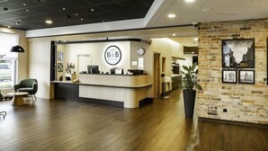 A hotel reception area with a modern design, featuring a reception desk, a clock, and a large potted plant. - B&B Hotel Torun (Torun)