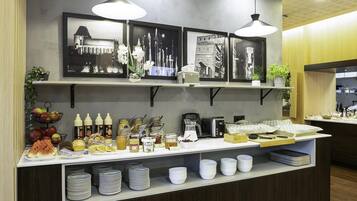 Una barra de desayuno con una variedad de alimentos y condimentos, como frutas, pasteles y bebidas. También hay cuadros enmarcados en la pared sobre la barra.