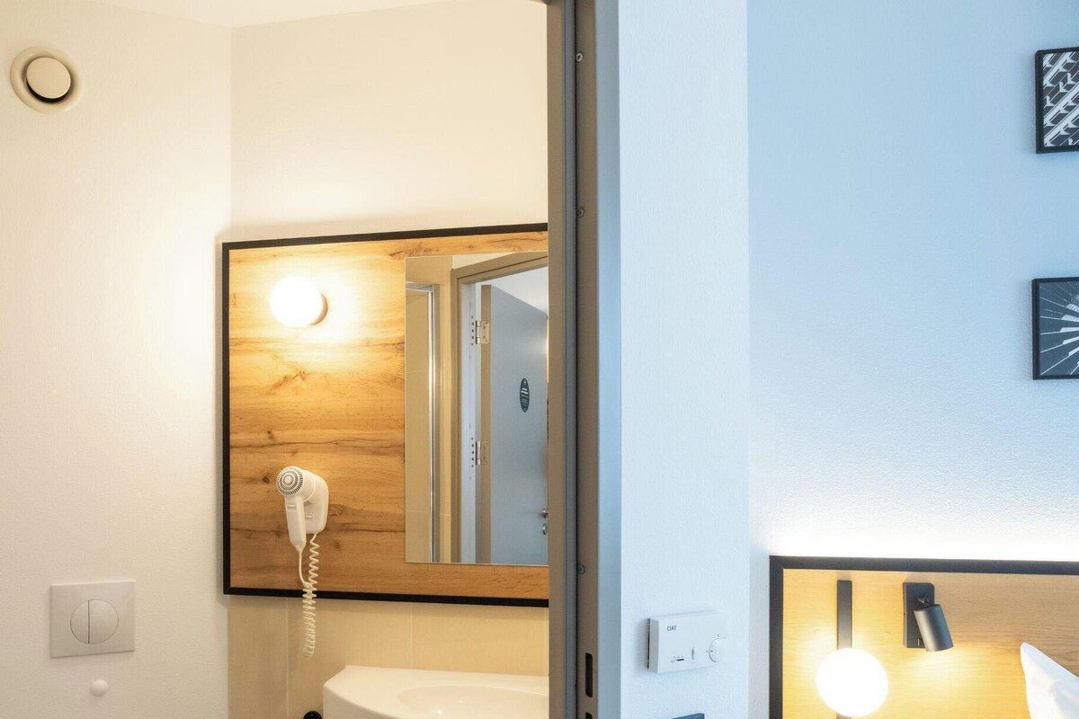 A bathroom with a wooden vanity, a white sink, a hairdryer, a mirror, and a light fixture.