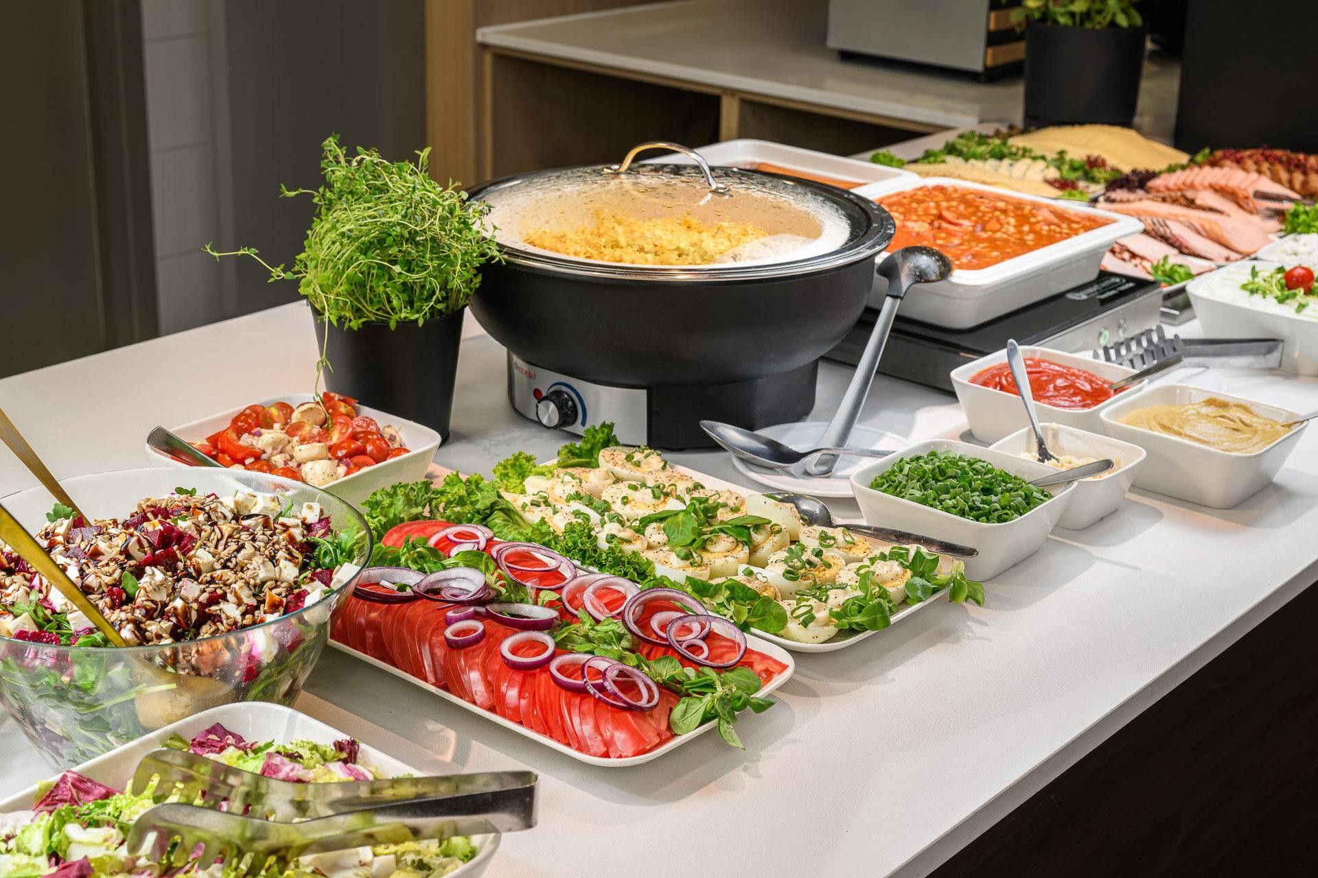 A buffet table with various dishes, including a pot of soup, salads, and sliced meats.