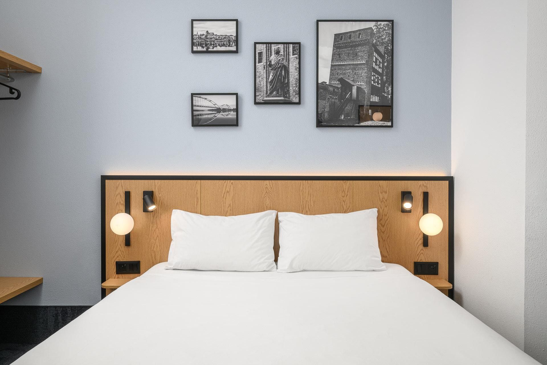 A hotel room with a bed, headboard, and wall-mounted artwork.
