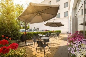 An outdoor patio with tables and chairs, umbrellas, and a building in the background. - B&B Hotel Torun (Torun)