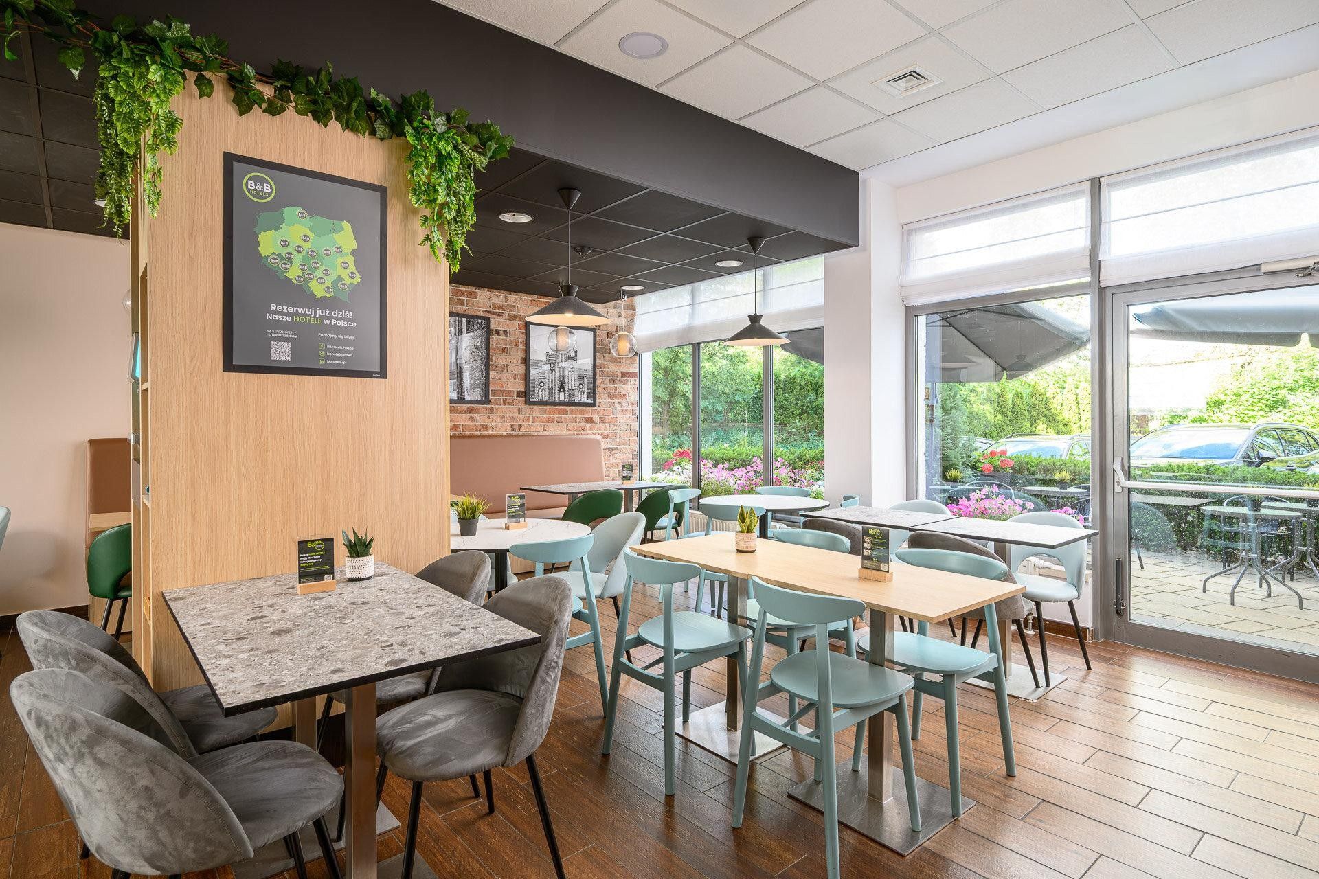 L’intérieur d’un restaurant, avec des tables et des chaises en bois, un mur en briques et une grande fenêtre donnant sur un jardin.